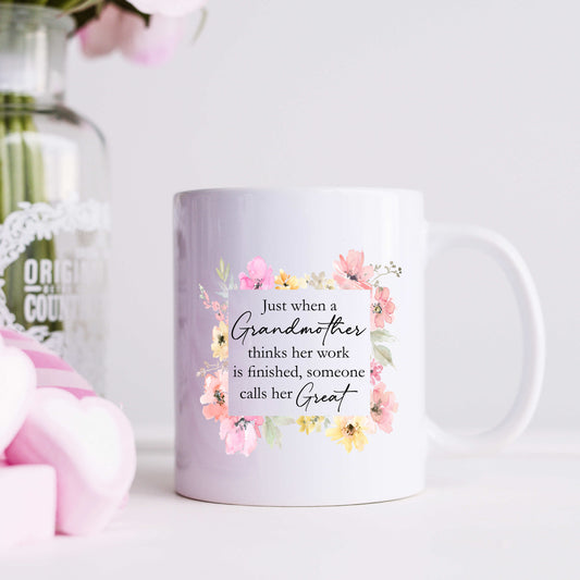 A white coffee mug with a floral print and text that reads, "Just when a grandmother thinks her work is finished, someone calls her Great"