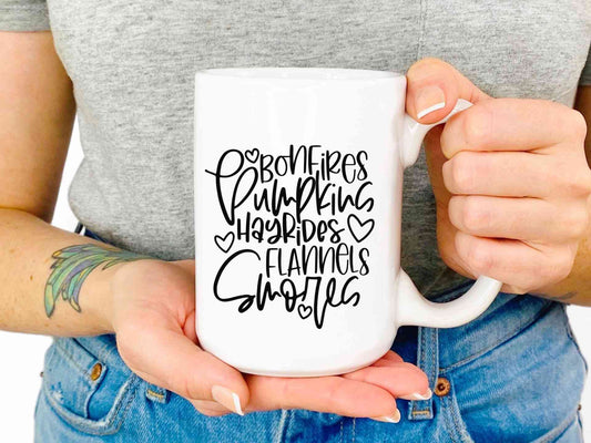 White mug printed with Bonfires, pumpkins, hayrides, flannels, smores in a script font.