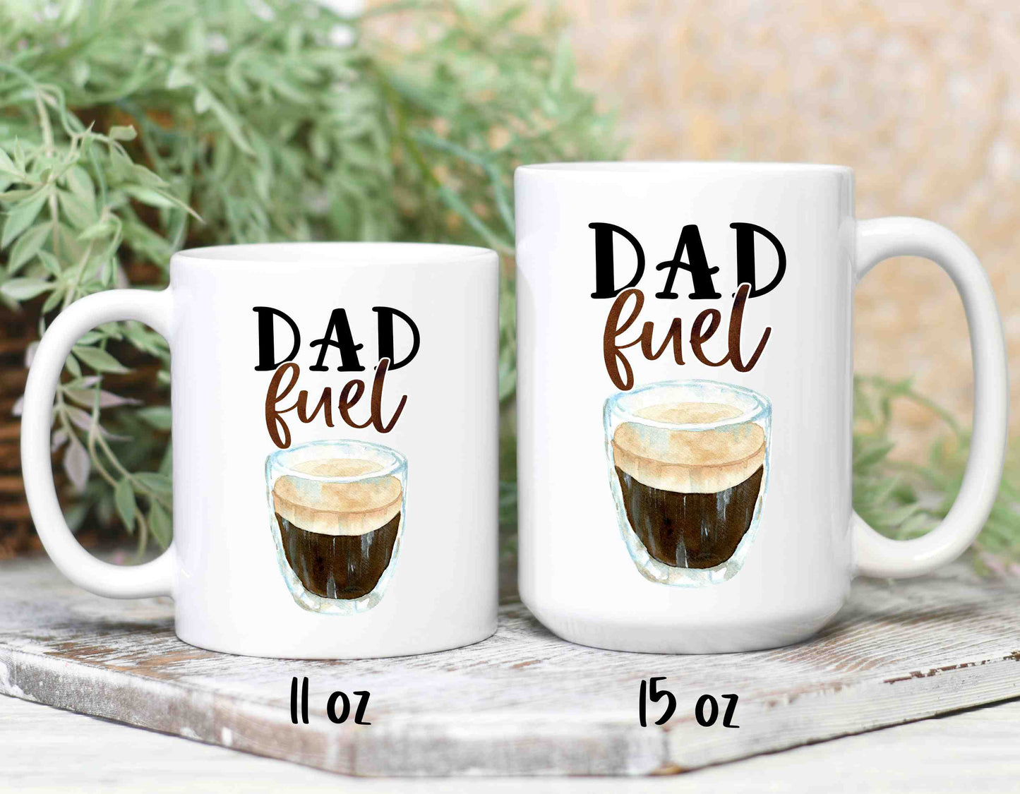 Two white coffee mugs reading dad fuel in script font. The mugs come in two sizes, 11oz and 15oz.