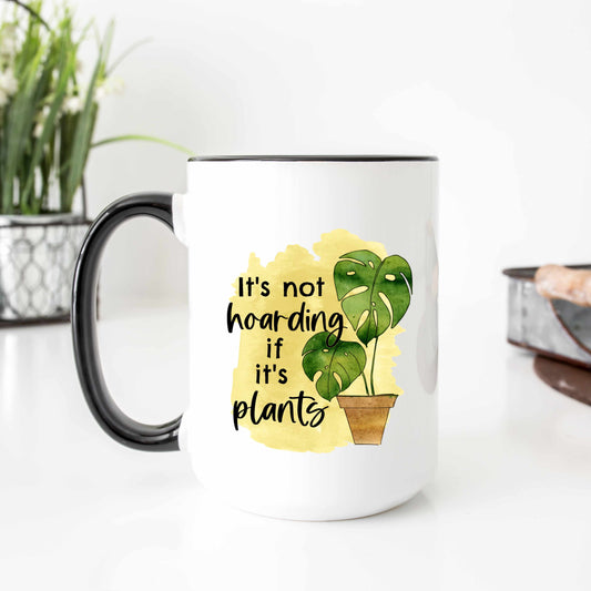 A white mug with a black handle with a picture of a potted monsterra that reads it's not hoarding if it's plants.