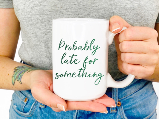 A closeup shot of a woman holding A white mug that reads "probably late for something" in a green script font
