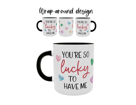 A white coffee mug with black handle printed with conversation hearts and the phrase "you're so lucky to have me". This photo shows the wrap-around design of the print.