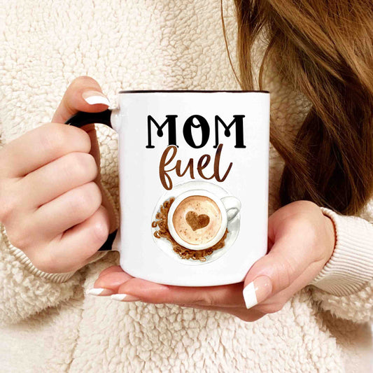 a closeup shot of a woman holding a white coffee mug that reads mom fuel in script font.