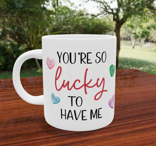 A white coffee mug printed with conversation hearts and the phrase "you're so lucky to have me"