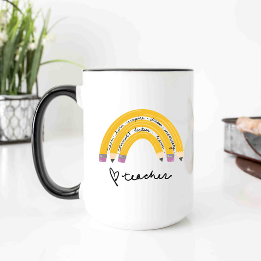 Adorable mug that makes a great teacher gift. A white mug with a rainbow made of pencils interspersed with motivational sayings. The mug has a hand drawn heart and teacher in a script font on the bottom. 